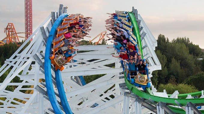 Riders on parallel tracks reaching for one another on Twisted Colossus.