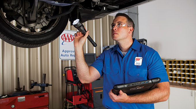 Mechanic inspecting the underside of a car at a AAA Approved Repair facility